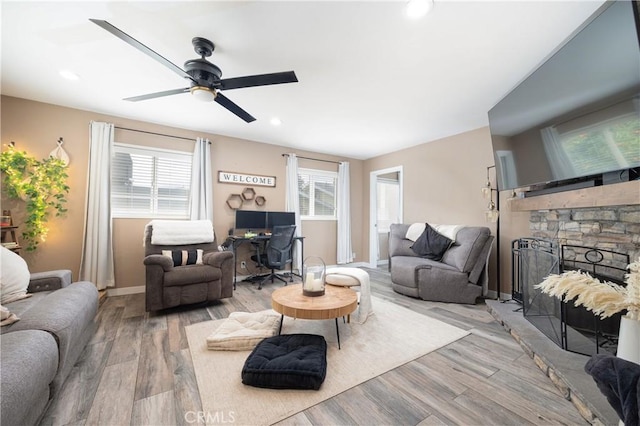 living room with a healthy amount of sunlight, a stone fireplace, and light hardwood / wood-style flooring