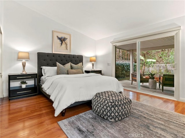 bedroom with wood-type flooring, vaulted ceiling, and access to outside