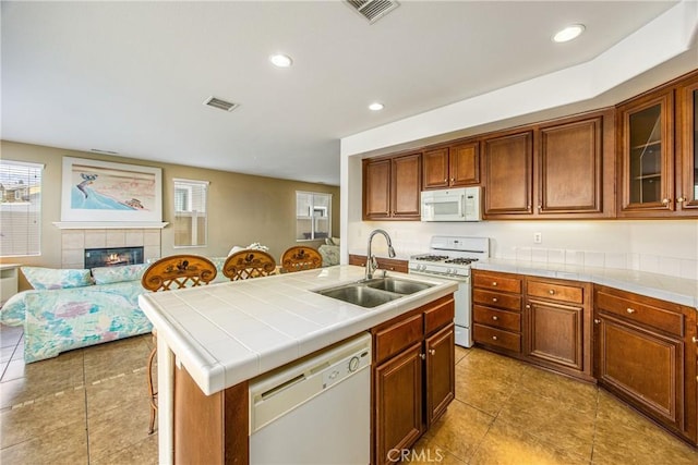 kitchen featuring sink, tile countertops, an island with sink, white appliances, and a fireplace