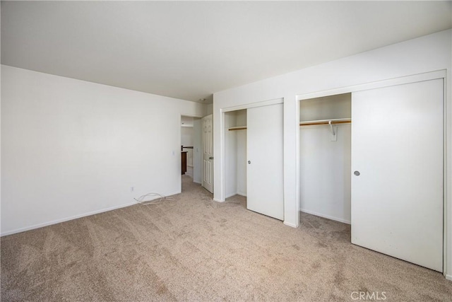 unfurnished bedroom featuring two closets and light colored carpet