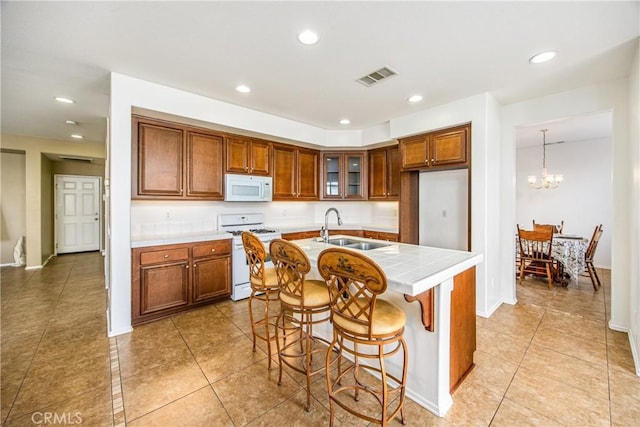 kitchen with pendant lighting, sink, white appliances, a breakfast bar area, and an island with sink