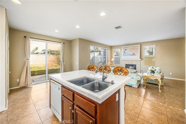 kitchen featuring sink, tile countertops, white dishwasher, a tile fireplace, and a kitchen island with sink