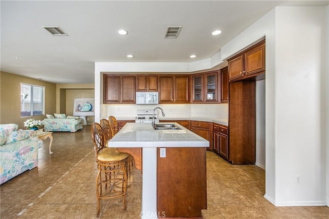 kitchen featuring sink, light tile patterned floors, a breakfast bar, a kitchen island with sink, and tile countertops