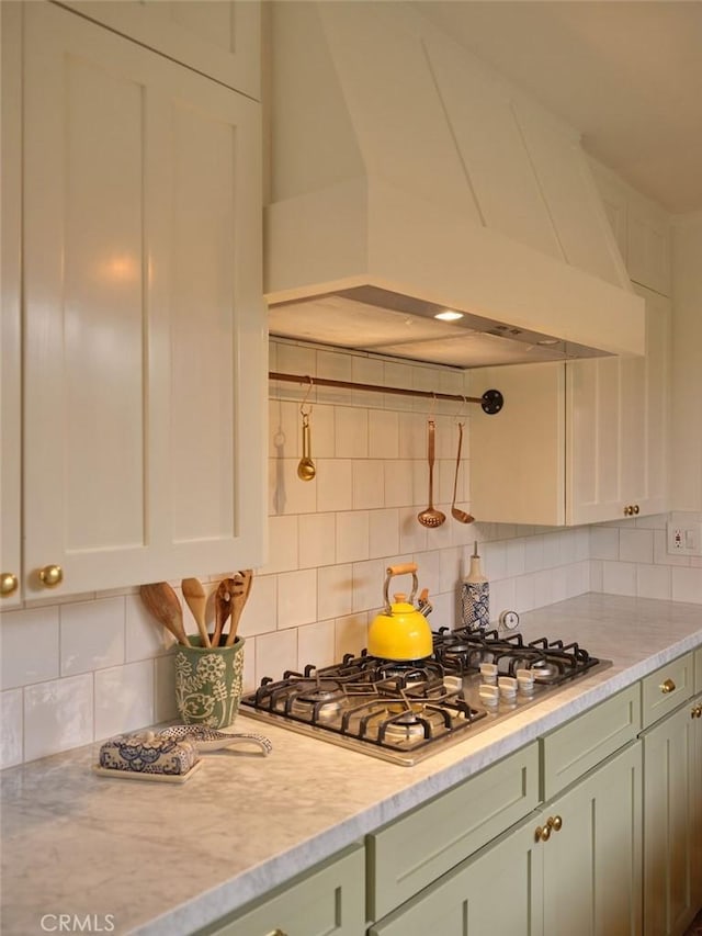 kitchen featuring premium range hood, backsplash, stainless steel gas stovetop, light stone countertops, and white cabinets