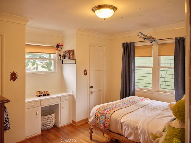 bedroom with crown molding, built in desk, and light hardwood / wood-style floors