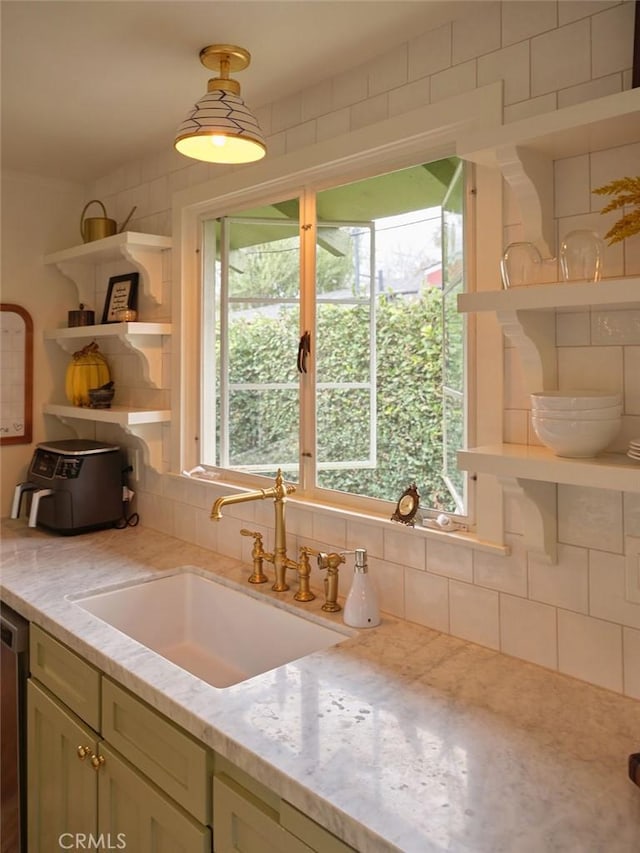 kitchen featuring hanging light fixtures, sink, stainless steel dishwasher, and light stone counters