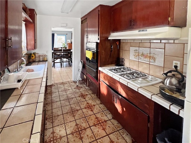 kitchen featuring sink, white gas stovetop, tile counters, oven, and backsplash