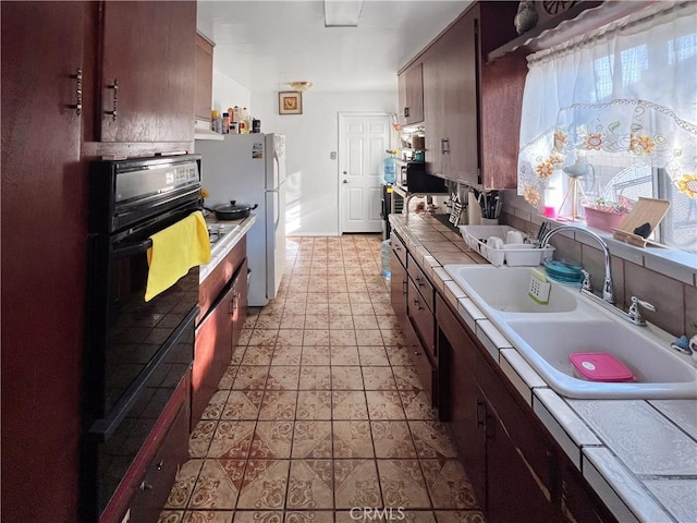 kitchen featuring tile countertops, sink, oven, white refrigerator, and dark brown cabinets