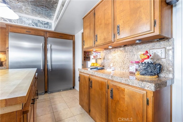 kitchen featuring built in refrigerator, tasteful backsplash, light stone countertops, and light tile patterned floors