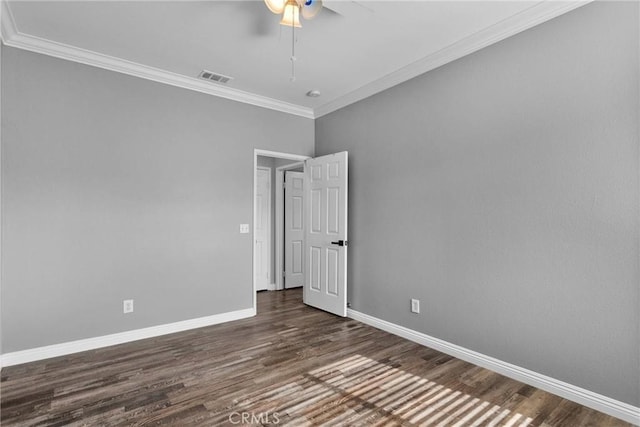 empty room featuring ornamental molding, dark wood finished floors, visible vents, and baseboards