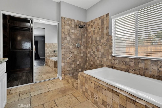 bathroom with a tile shower, a wealth of natural light, stone tile flooring, and a garden tub