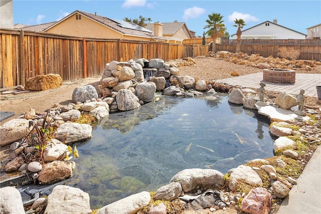 exterior space featuring a small pond, a fenced backyard, and an outdoor fire pit