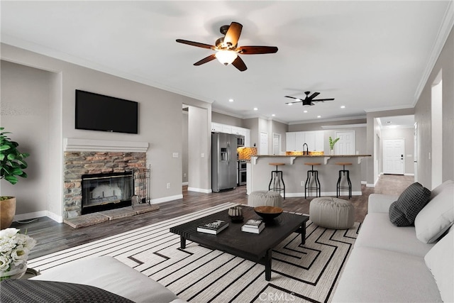 living room with recessed lighting, dark wood-style flooring, a fireplace, baseboards, and crown molding