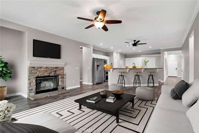 living room featuring crown molding, a stone fireplace, dark hardwood / wood-style floors, and sink