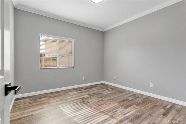 spare room featuring wood finished floors, crown molding, and baseboards