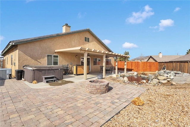 rear view of house featuring a chimney, a fire pit, a fenced backyard, a hot tub, and a patio