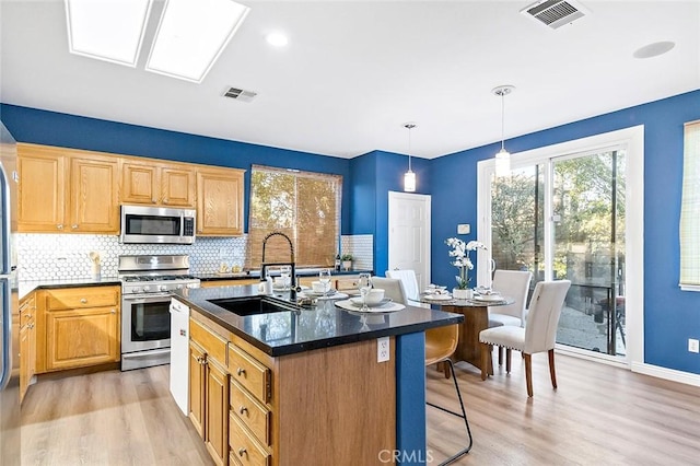 kitchen with sink, appliances with stainless steel finishes, hanging light fixtures, an island with sink, and decorative backsplash