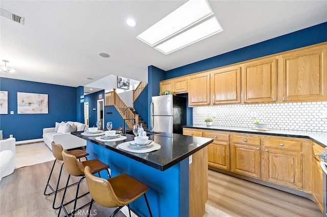 kitchen with light hardwood / wood-style flooring, stainless steel fridge, a kitchen breakfast bar, and a center island