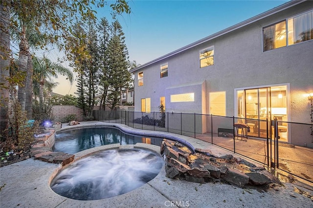 pool at dusk with an in ground hot tub