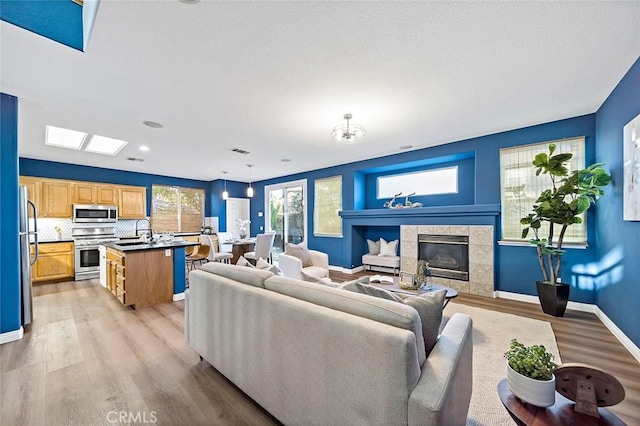 living room with a tiled fireplace, sink, a skylight, and light wood-type flooring