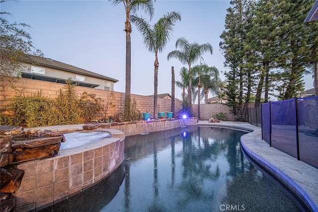 pool at dusk featuring an in ground hot tub