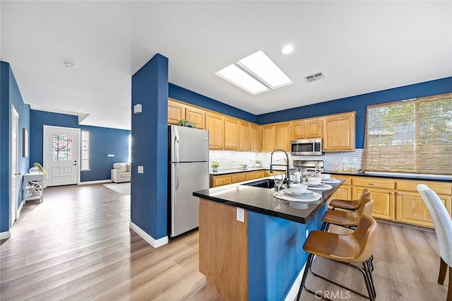 kitchen with a breakfast bar, sink, a skylight, an island with sink, and stainless steel appliances