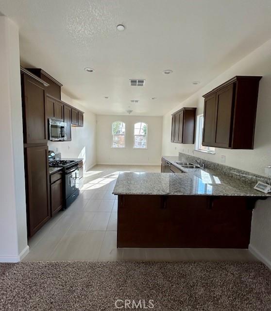 kitchen with a kitchen breakfast bar, light stone countertops, light tile patterned flooring, black range with gas stovetop, and kitchen peninsula