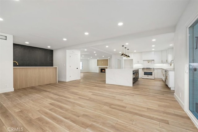 kitchen with sink, white cabinetry, stainless steel stove, a kitchen island, and pendant lighting