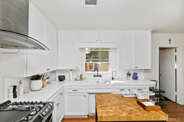 kitchen featuring butcher block countertops, sink, white cabinets, gas range, and wall chimney exhaust hood