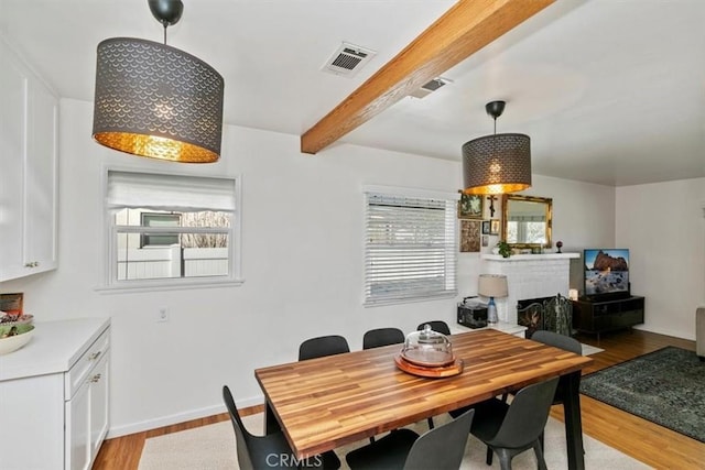 dining space featuring light hardwood / wood-style flooring, a fireplace, and beamed ceiling