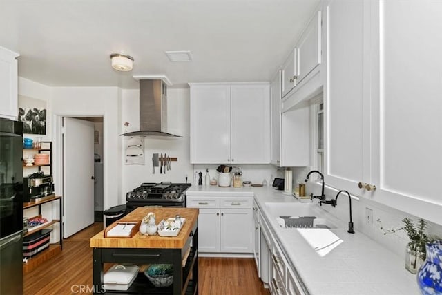 kitchen featuring white cabinetry, sink, wooden counters, stainless steel gas range oven, and wall chimney range hood