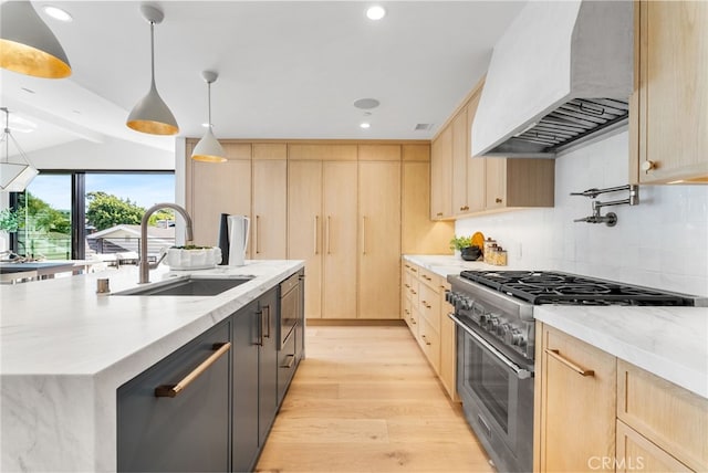 kitchen featuring sink, decorative light fixtures, an island with sink, stainless steel stove, and custom range hood