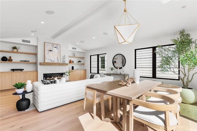 dining space with vaulted ceiling with beams, a large fireplace, and light hardwood / wood-style flooring