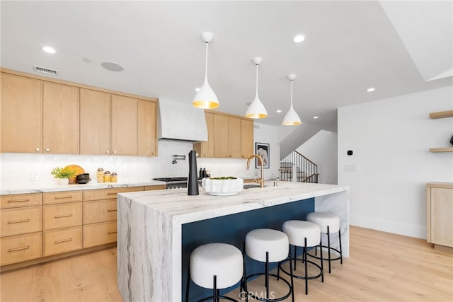 kitchen featuring pendant lighting, custom exhaust hood, a center island with sink, and light brown cabinets