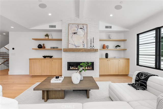 living room with lofted ceiling with beams, a brick fireplace, and light hardwood / wood-style flooring