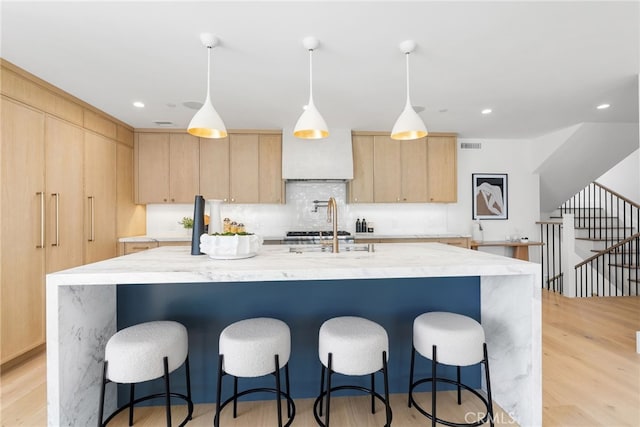 kitchen with hanging light fixtures, an island with sink, light brown cabinetry, and light hardwood / wood-style floors