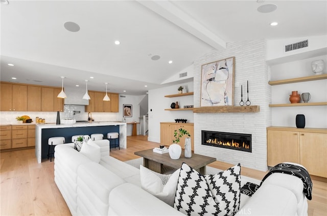 living room with light hardwood / wood-style flooring, lofted ceiling with beams, and a large fireplace