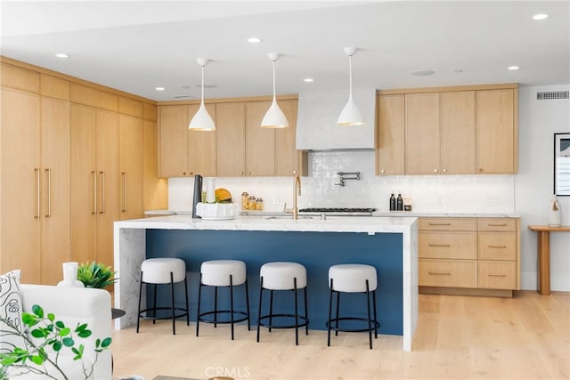 kitchen featuring light brown cabinetry, hanging light fixtures, backsplash, and a kitchen bar