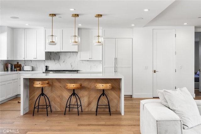 kitchen featuring tasteful backsplash, light countertops, hanging light fixtures, white cabinets, and a kitchen bar