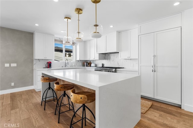 kitchen featuring decorative light fixtures, light countertops, white cabinetry, a kitchen island, and range