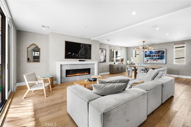 living room with an inviting chandelier, light hardwood / wood-style flooring, and a tiled fireplace