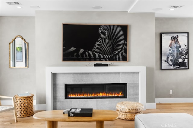 room details with a tile fireplace, visible vents, baseboards, and wood finished floors