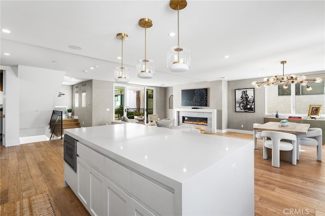 kitchen with light wood-style floors, white cabinets, light countertops, a glass covered fireplace, and decorative light fixtures