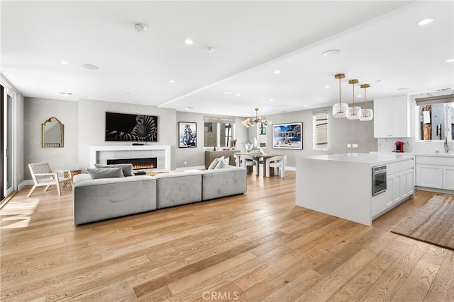 living room with a warm lit fireplace, a healthy amount of sunlight, a notable chandelier, and light wood finished floors