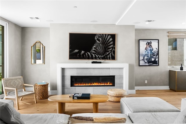 living room featuring baseboards, a glass covered fireplace, visible vents, and light wood-style floors