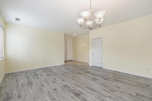 spare room featuring a notable chandelier and light wood-type flooring