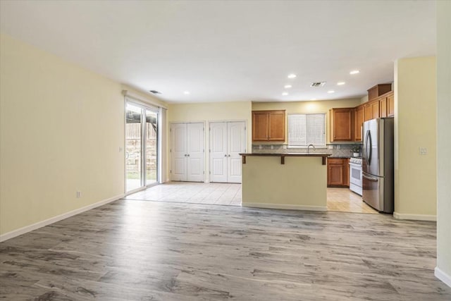 kitchen with a kitchen island, stainless steel refrigerator, backsplash, a kitchen breakfast bar, and light hardwood / wood-style floors