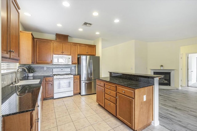 kitchen featuring sink, white appliances, dark stone counters, and a kitchen island