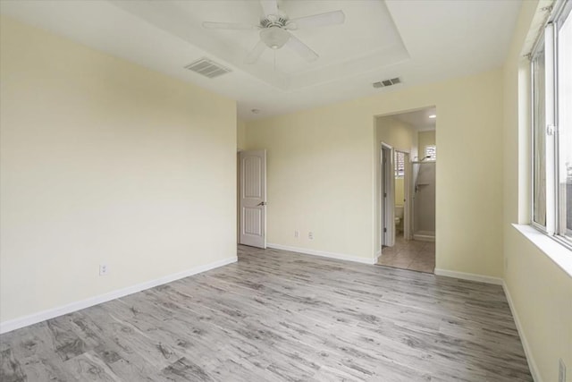 empty room with ceiling fan, light hardwood / wood-style floors, and a tray ceiling