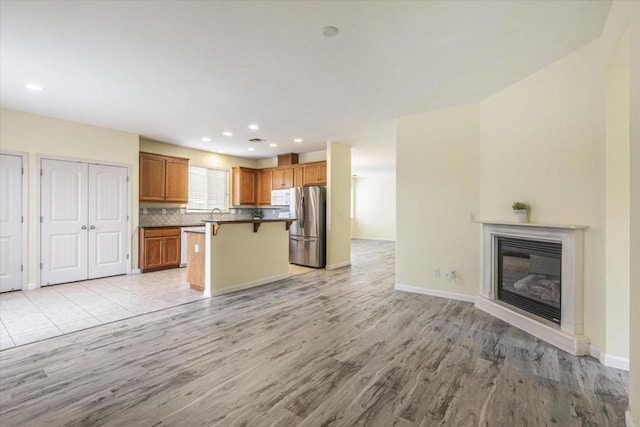 kitchen featuring a breakfast bar area, a center island, light hardwood / wood-style flooring, stainless steel refrigerator, and decorative backsplash